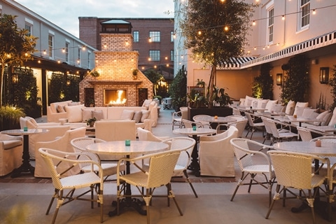 A cozy, outdoor event space with neutral colors, string lights and a fireplace.